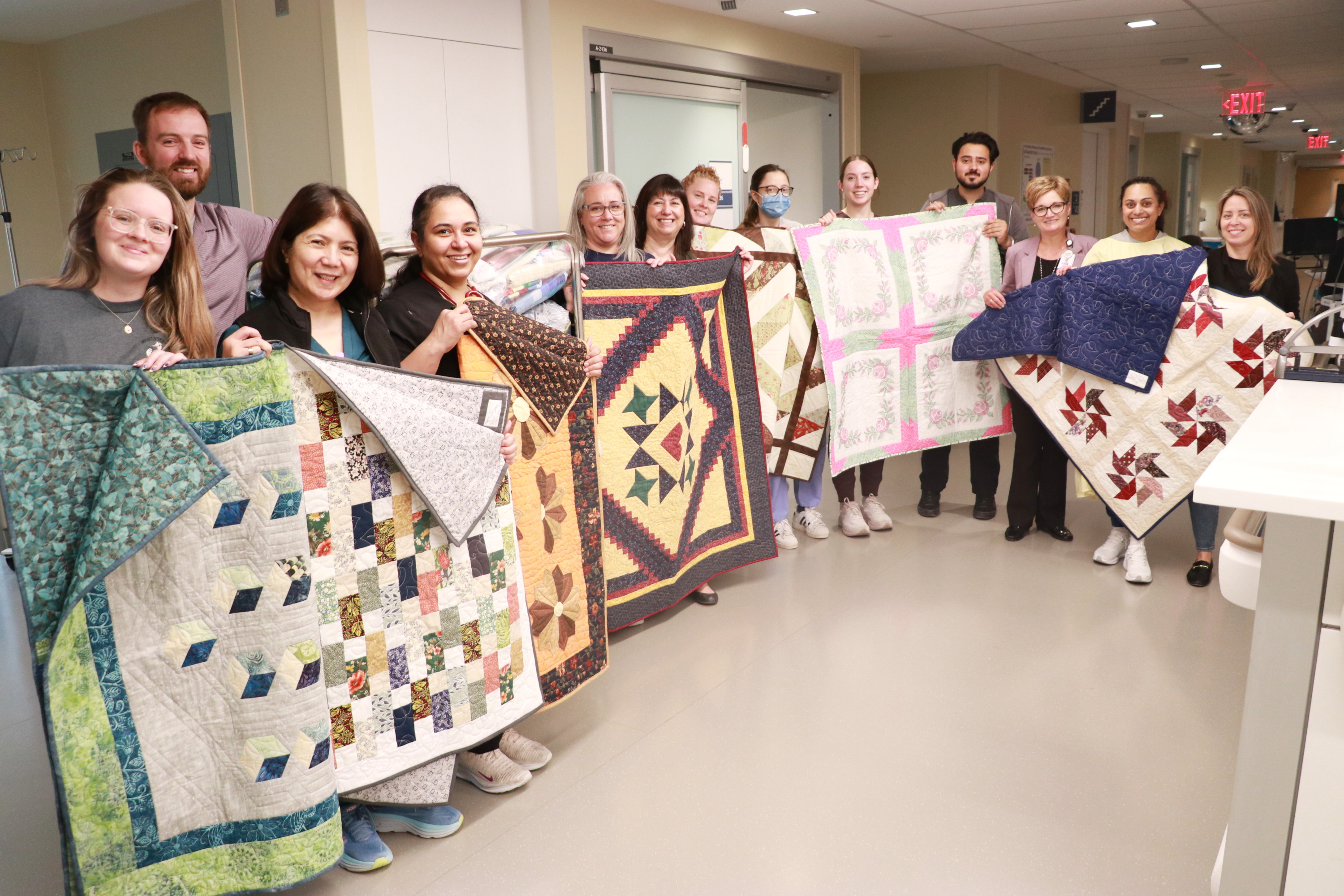 ICU staff hold up donated quilts in various shapes and patterns.
