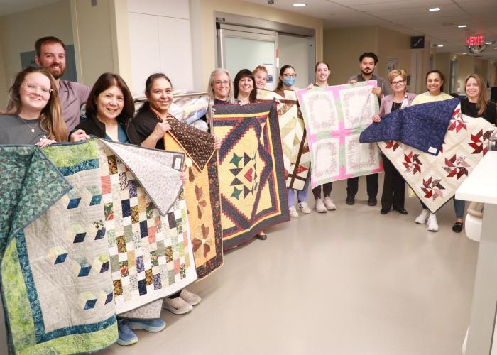 ICU staff hold up donated quilts in various shapes and patterns.
